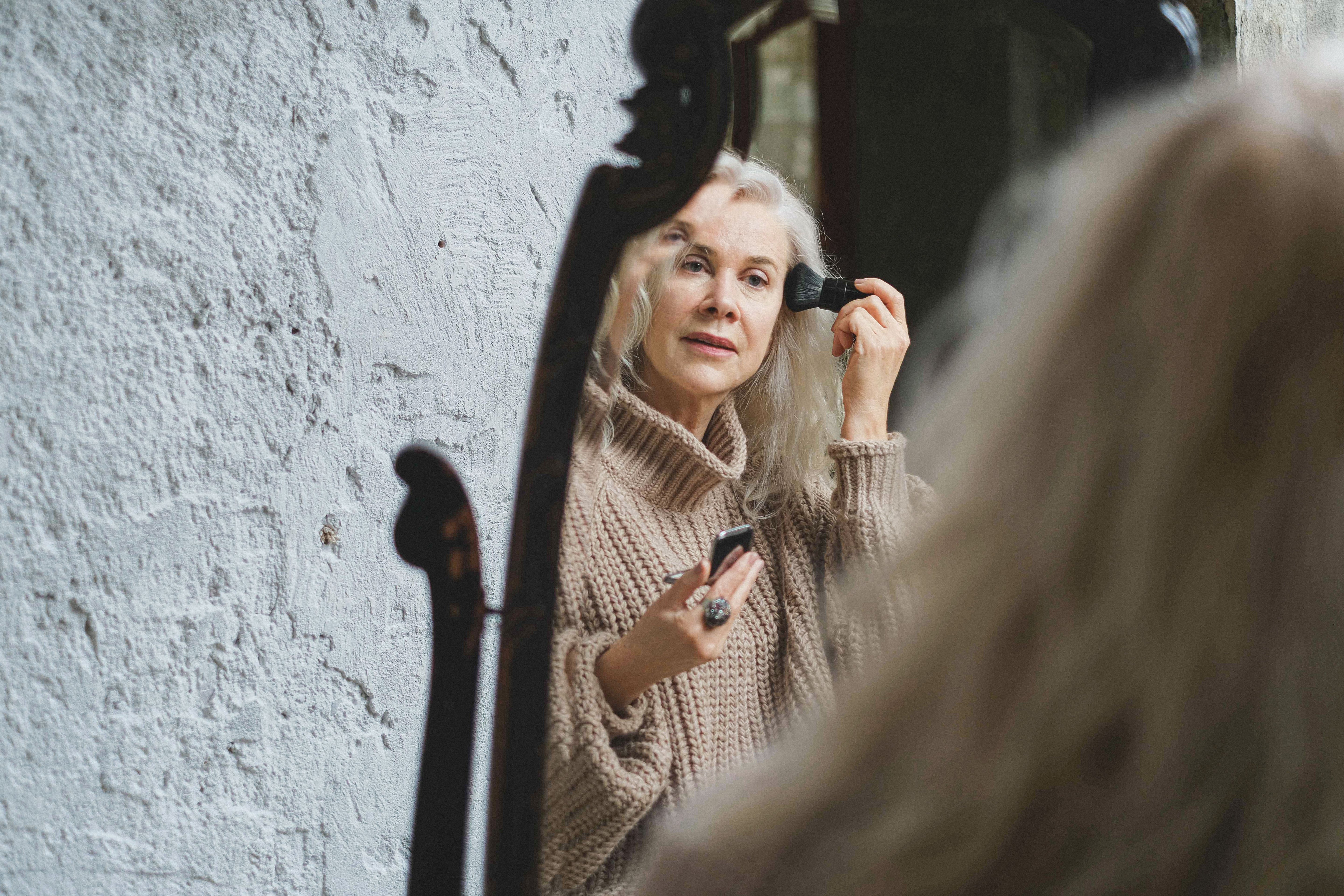 Mature woman applying makeup while looking into a mirror